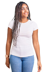 Obraz premium Young african american woman with braids wearing casual clothes looking away to side with smile on face, natural expression. laughing confident.