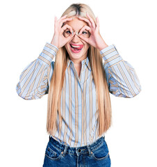 Beautiful blonde woman wearing casual striped shirt doing ok gesture like binoculars sticking tongue out, eyes looking through fingers. crazy expression.