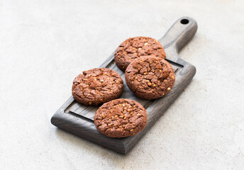 Vegan Cocoa oatmeal cookies with crushed peanuts on a wooden board. Light gray background. Rustic style