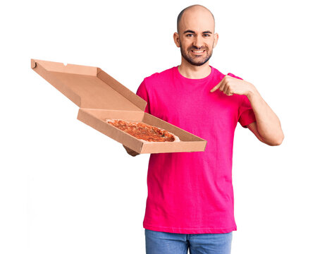 Young handsome man holding delivery pizza cardboard box pointing finger to one self smiling happy and proud