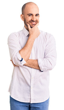 Young handsome man wearing elegant shirt looking confident at the camera smiling with crossed arms and hand raised on chin. thinking positive.