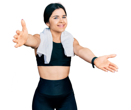 Young brunette woman with blue eyes wearing sportswear and towel looking at the camera smiling with open arms for hug. cheerful expression embracing happiness.