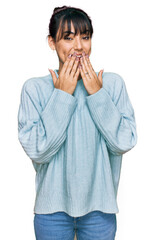 Young hispanic woman wearing casual clothes laughing and embarrassed giggle covering mouth with...