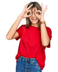 Obraz na płótnie Canvas Teenager caucasian girl wearing casual red t shirt doing ok gesture like binoculars sticking tongue out, eyes looking through fingers. crazy expression.