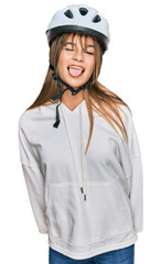 Teenager caucasian girl wearing bike helmet sticking tongue out happy with funny expression. emotion concept.