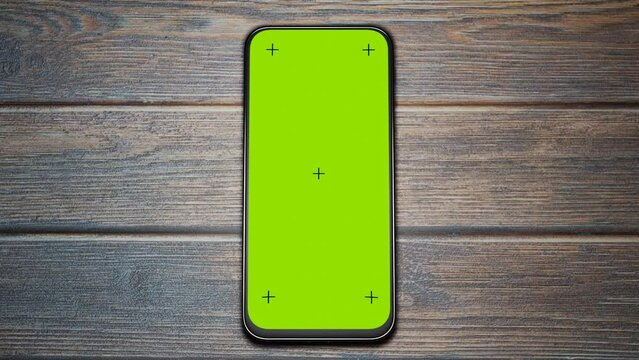 The movement of the camera around the green screen of the smartphone. Phone on a wooden table. Green chromakey with crosses on the phone screen. Template for your website design, application, interfac