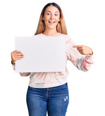 Beautiful young woman holding blank empty banner smiling happy pointing with hand and finger