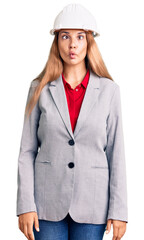 Beautiful young woman wearing architect hardhat making fish face with lips, crazy and comical gesture. funny expression.