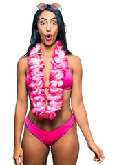 Beautiful hispanic woman wearing bikini and hawaiian lei afraid and shocked with surprise...