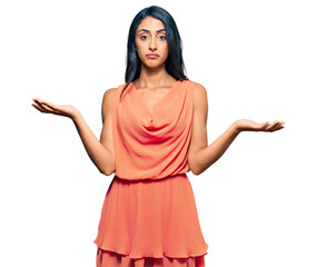 Beautiful hispanic woman wearing summer dress clueless and confused expression with arms and hands...