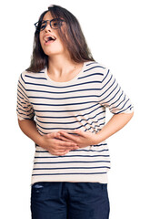 Brunette teenager girl wearing casual clothes and glasses with hand on stomach because nausea, painful disease feeling unwell. ache concept.