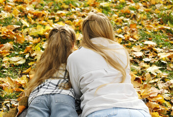 Fototapeta premium The family has fun in the park. The girl and mother lie on a blanket with their backs to the camera and look at the autumn leaves.