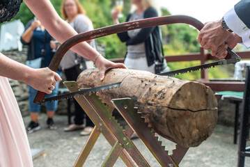 Young bridal couple groom bride sawing a tree trunk together german wedding tradition