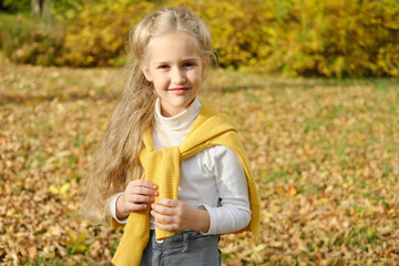 Little blonde preschool girl in jeans, turtleneck and sweater posing for the camera in the autumn park