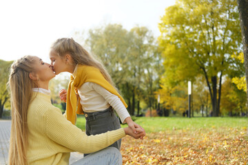Fototapeta premium young blonde mother kneeling and kissing the preschooler daughter in the park on a sunny day