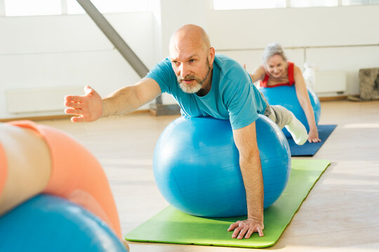 Group of mature friends jumping on blue fitball on yoga class