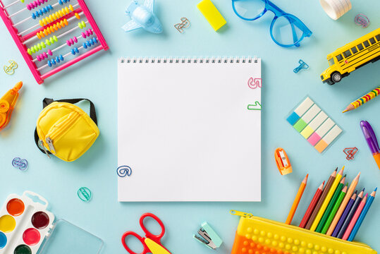 Embark on a learning adventure with this creative top view composition: colorful collection of childish school supplies on serene pastel blue surface, with blank notebook page for text or advertising