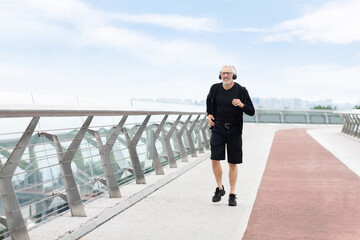 Happy elderly man jogging outside by bridge, copy space