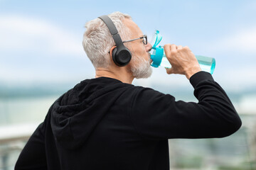 Fototapeta premium Closeup of elderly sportsman drinking water during workout outdoors