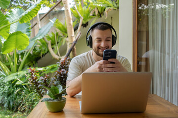Young happy creative freelancer man in casual clothes working in coworking space wearing headphones...