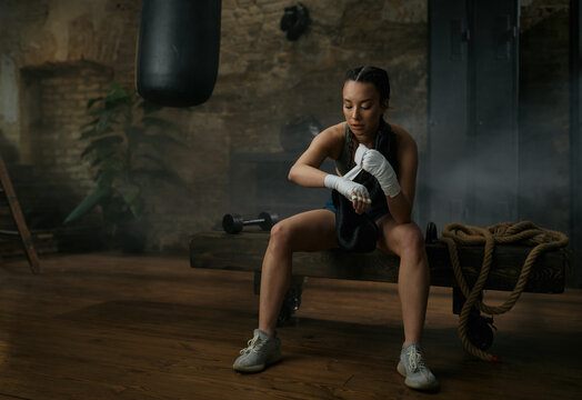 Athletic young female boxer wrapping bandages on her hands