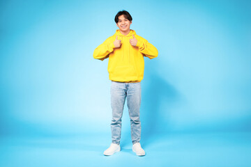 Asian guy gesturing thumbs up with both hands, blue background