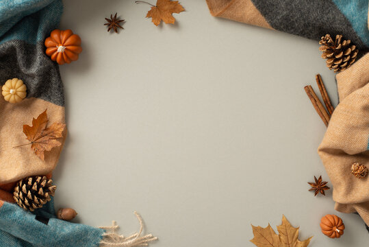 Capture the essence of homey autumn comfort with this top view photo. Patchy blanket, pumpkin candles, pinecones, spices and maple leaves on grey backdrop provide inviting atmosphere for text/advert