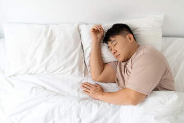 Top view of peaceful asian man sleeping in comfy bed