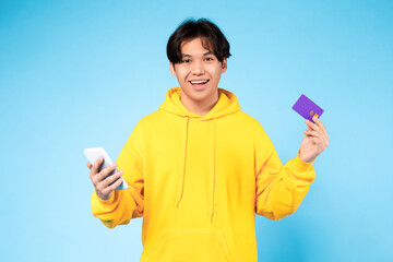 Smiling japanese guy using cellphone and credit card, blue background