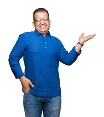 Middle age arab man wearing glasses over isolated background smiling cheerful presenting and pointing with palm of hand looking at the camera.