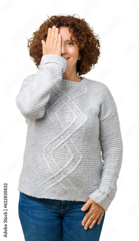 Sticker Beautiful middle ager senior woman wearing winter sweater over isolated background covering one eye with hand with confident smile on face and surprise emotion.