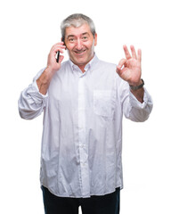 Handsome senior man talking on smartphone over isolated background doing ok sign with fingers, excellent symbol