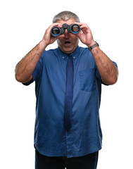 Handsome senior man looking through binoculars over isolated background scared in shock with a surprise face, afraid and excited with fear expression