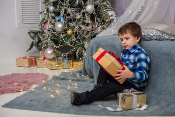 a little boy sits next to a christmas tree and gifts.