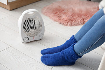Woman warming legs in socks near electric fan heater at home, closeup