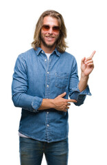 Young handsome man with long hair wearing sunglasses over isolated background with a big smile on face, pointing with hand and finger to the side looking at the camera.