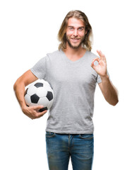 Young handsome man with long hair over isolated background holding football ball doing ok sign with fingers, excellent symbol