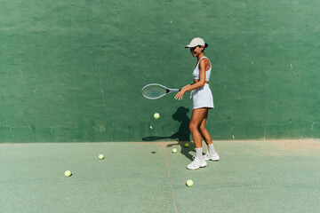 beautiful girl in a cap plays tennis on the tennis court against the background of a green wall