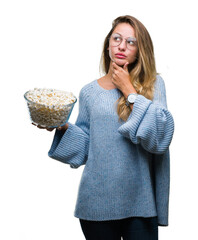 Young beautiful blonde woman eating popcorn over isolated background serious face thinking about...