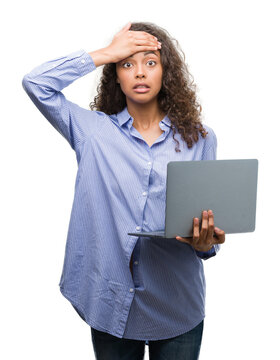 Young hispanic woman holding computer laptop stressed with hand on head, shocked with shame and surprise face, angry and frustrated. Fear and upset for mistake.
