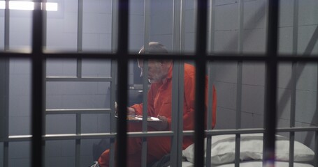 Elderly prisoner in orange uniform sits in prison cell, eats food. Criminal serves imprisonment...