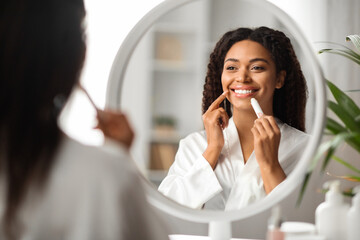 Beautiful Black Lady Looking At Mirror And Applying Moisturising Lip Balm