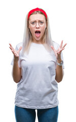 Obraz na płótnie Canvas Young blonde woman wearing glasses over isolated background crazy and mad shouting and yelling with aggressive expression and arms raised. Frustration concept.