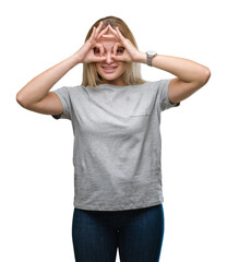 Young caucasian woman over isolated background doing ok gesture like binoculars sticking tongue out, eyes looking through fingers. Crazy expression.