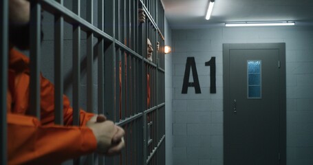 Elderly prisoner in orange uniform stretches fingers, leans on metal bars. Criminal serves...