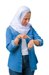 Middle age eastern arab woman wearing arabian hijab over isolated background Checking the time on...