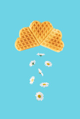 Flowers fly out of heart-shaped cookie clouds. Blue background. Minimal creative, surreal, food and flowers concept.