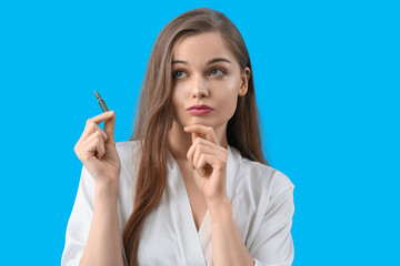 Obraz premium Beautiful thoughtful woman with ampule on blue background. Skin care concept