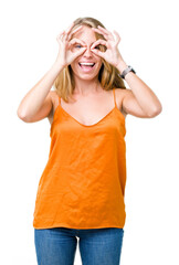 Beautiful young woman wearing orange shirt over isolated background doing ok gesture like binoculars sticking tongue out, eyes looking through fingers. Crazy expression.