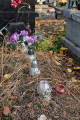 All Saints Day. Candles on graves. Autumn and leaves between candles on the graves of the dead in the cemetery. - obrazy, fototapety, plakaty